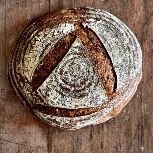 Runt surdegsbröd med rustik skorpa och mjölmönster på träbord